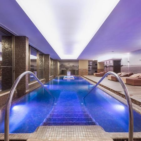 Ap Lago Montargil - Conference & Spa エクステリア 写真 The photo shows a modern indoor swimming pool area. The pool features a sleek design with steps leading into the water and a gentle curve at the sides. The water is illuminated in a blue hue, enhancing the relaxing atmosphere. Surrounding the pool ar