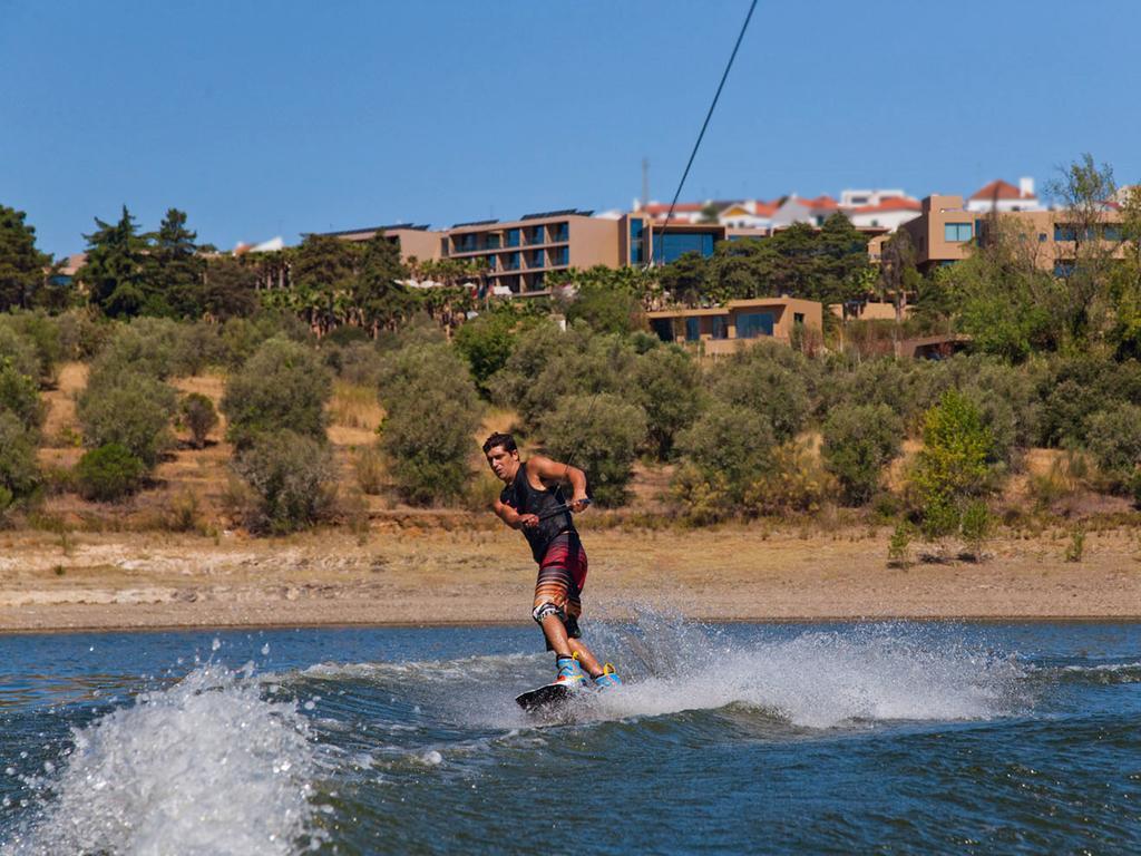 Ap Lago Montargil - Conference & Spa エクステリア 写真 The photo shows a person wakeboarding on a body of water. The individual is being pulled by a cable, which is likely connected to a boat or a winch. The person is wearing a life jacket and swim shorts, balancing on the board as they enjoy the activit