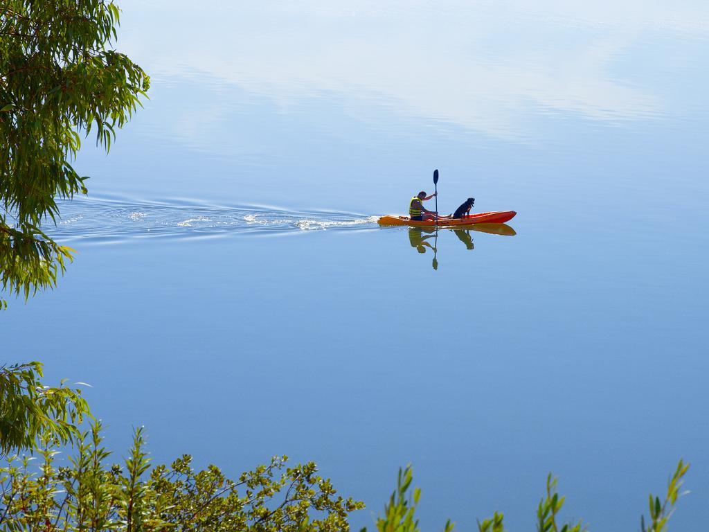 Ap Lago Montargil - Conference & Spa エクステリア 写真 The photo shows a serene scene of a person kayaking on a calm body of water. The surface of the water is very smooth, reflecting the surroundings, and there is a gentle wake behind the kayak indicating movement. The kayaker is wearing a life jacket a