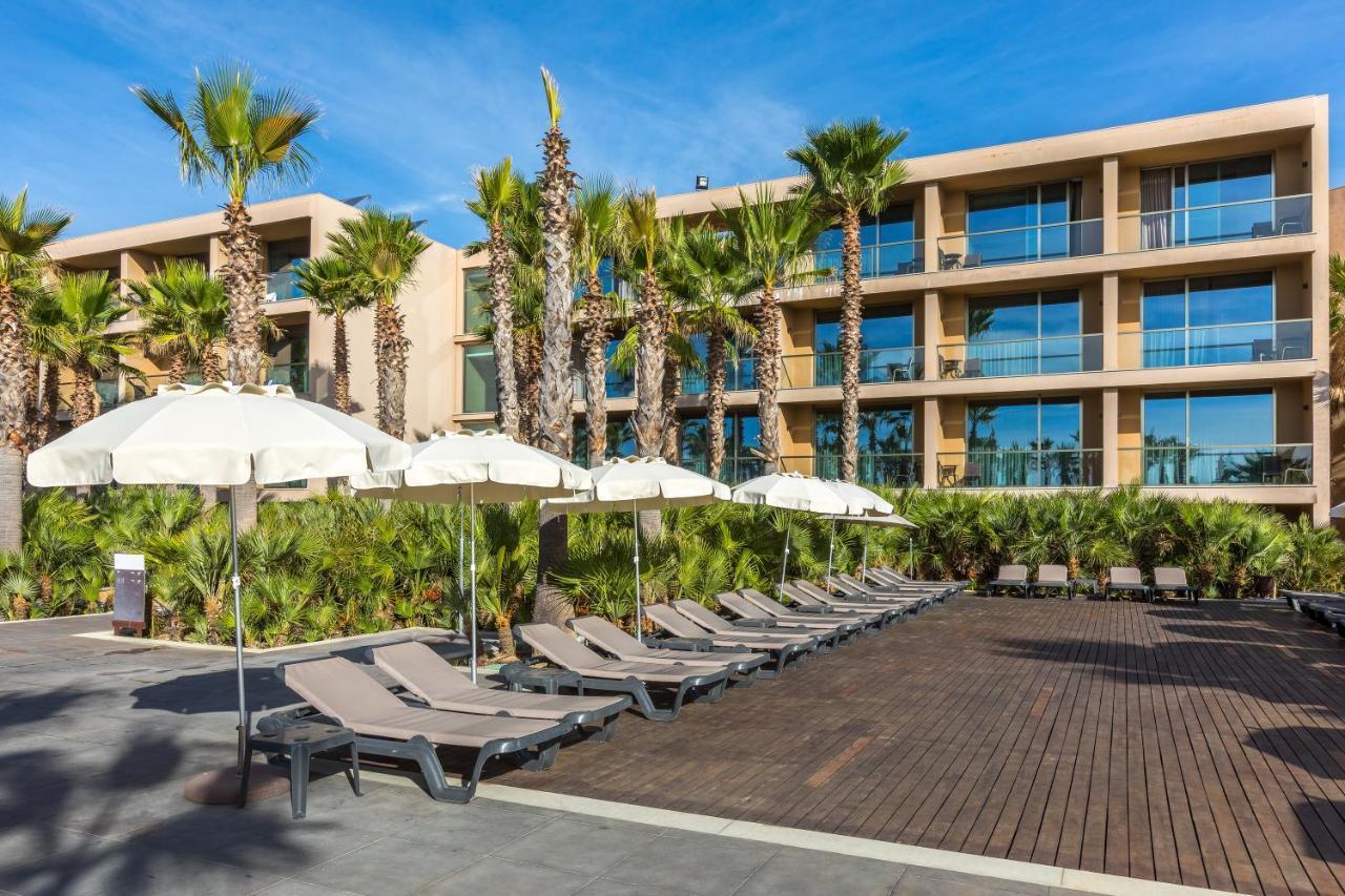 Ap Lago Montargil - Conference & Spa エクステリア 写真 The photo shows a modern resort or hotel area featuring several lounge chairs lined up on a wooden deck. Each lounge chair is paired with a white umbrella, providing shade. In the background, there are palm trees, which add to the tropical atmosphere