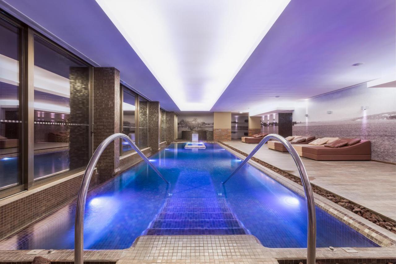Ap Lago Montargil - Conference & Spa エクステリア 写真 The photo shows a modern indoor swimming pool area. The pool features a sleek design with steps leading into the water and a gentle curve at the sides. The water is illuminated in a blue hue, enhancing the relaxing atmosphere. Surrounding the pool ar