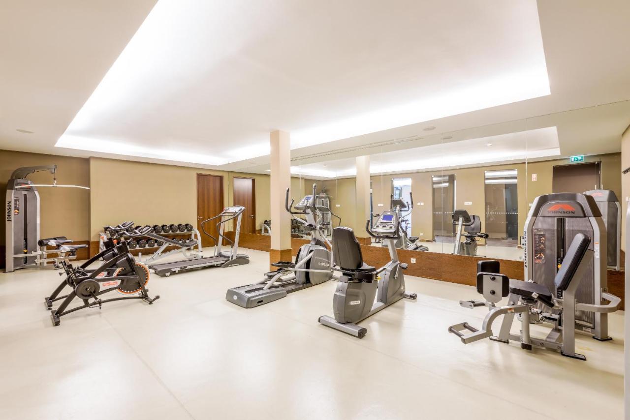 Ap Lago Montargil - Conference & Spa エクステリア 写真 The image shows a modern gym interior featuring various exercise equipment. On the left, there are free weights and weight benches. In the center, there are multiple machines, including a stationary bike and an elliptical. The space is well-lit with 