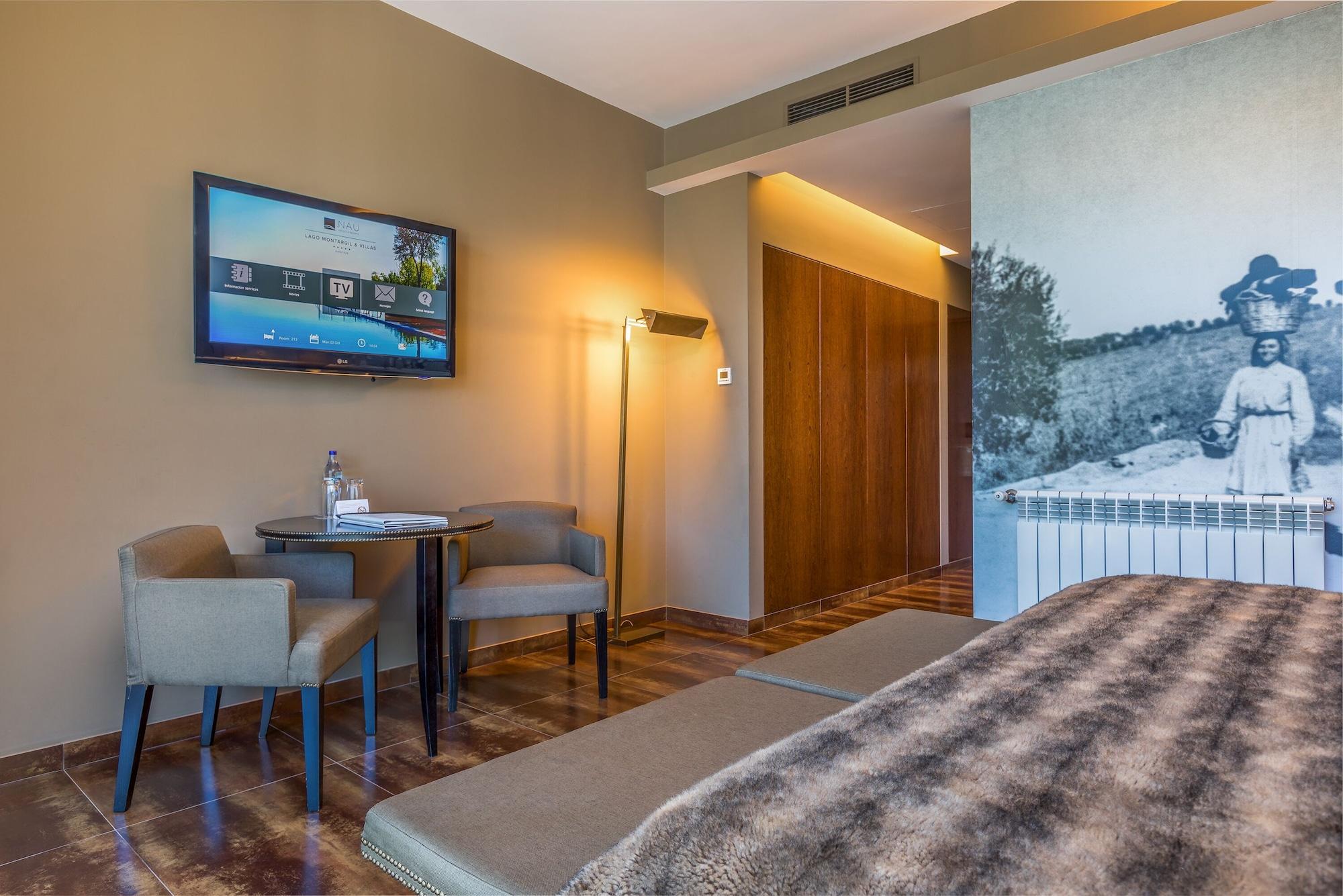 Ap Lago Montargil - Conference & Spa エクステリア 写真 The photo shows an interior of a room, likely a hotel or a modern living space. In the foreground, there is a bed with a textured brown blanket. To one side, there are two comfortable chairs and a small table, possibly with a bottle of water. A flat-