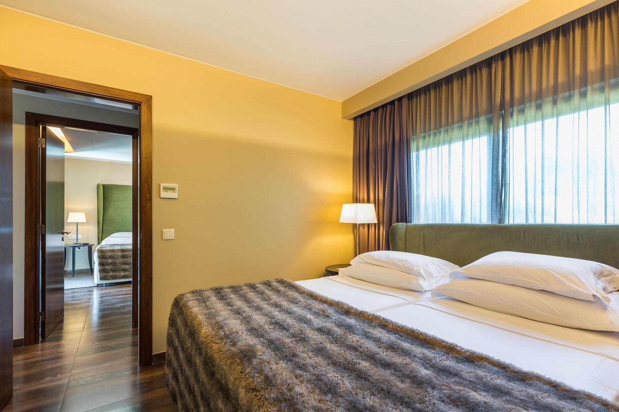Ap Lago Montargil - Conference & Spa エクステリア 写真 The photo shows the interior of a well-furnished hotel room. It features two beds with white linens and a gray decorative throw on top. The walls are painted a warm yellow, and there are floor-to-ceiling windows covered with dark curtains that allow 