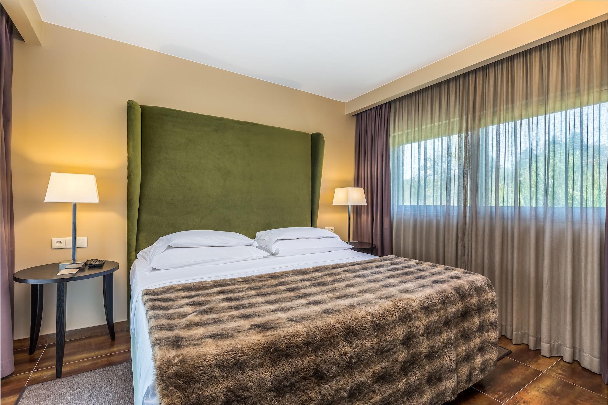 Ap Lago Montargil - Conference & Spa エクステリア 写真 The photo shows a cozy hotel room featuring a large bed with two white pillows and a fur-style blanket draped over it. Behind the bed is a tall, green headboard that adds a touch of color to the room. On either side of the bed are bedside tables, eac