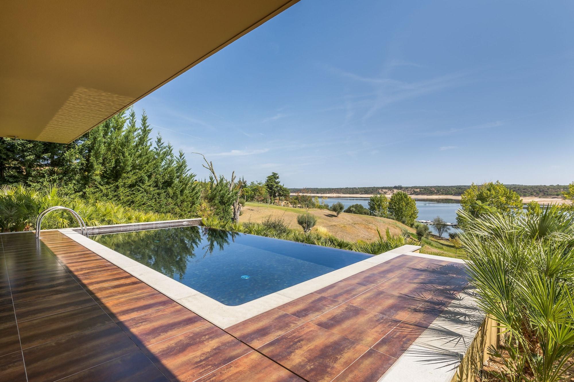 Ap Lago Montargil - Conference & Spa エクステリア 写真 The photo shows a luxurious infinity pool situated on a terrace or deck. The pool features a sleek, modern design with a dark blue surface that reflects the surrounding scenery. In the background, there is a landscape of rolling hills and a body of w