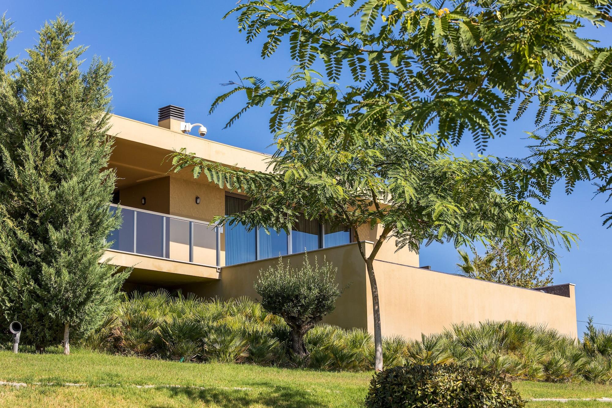 Ap Lago Montargil - Conference & Spa エクステリア 写真 The photo showcases a modern house situated on a grassy slope. The house features a light-colored exterior with large windows and a balcony. Surrounding the building are several trees and landscaping that enhances the natural environment. The sky is 