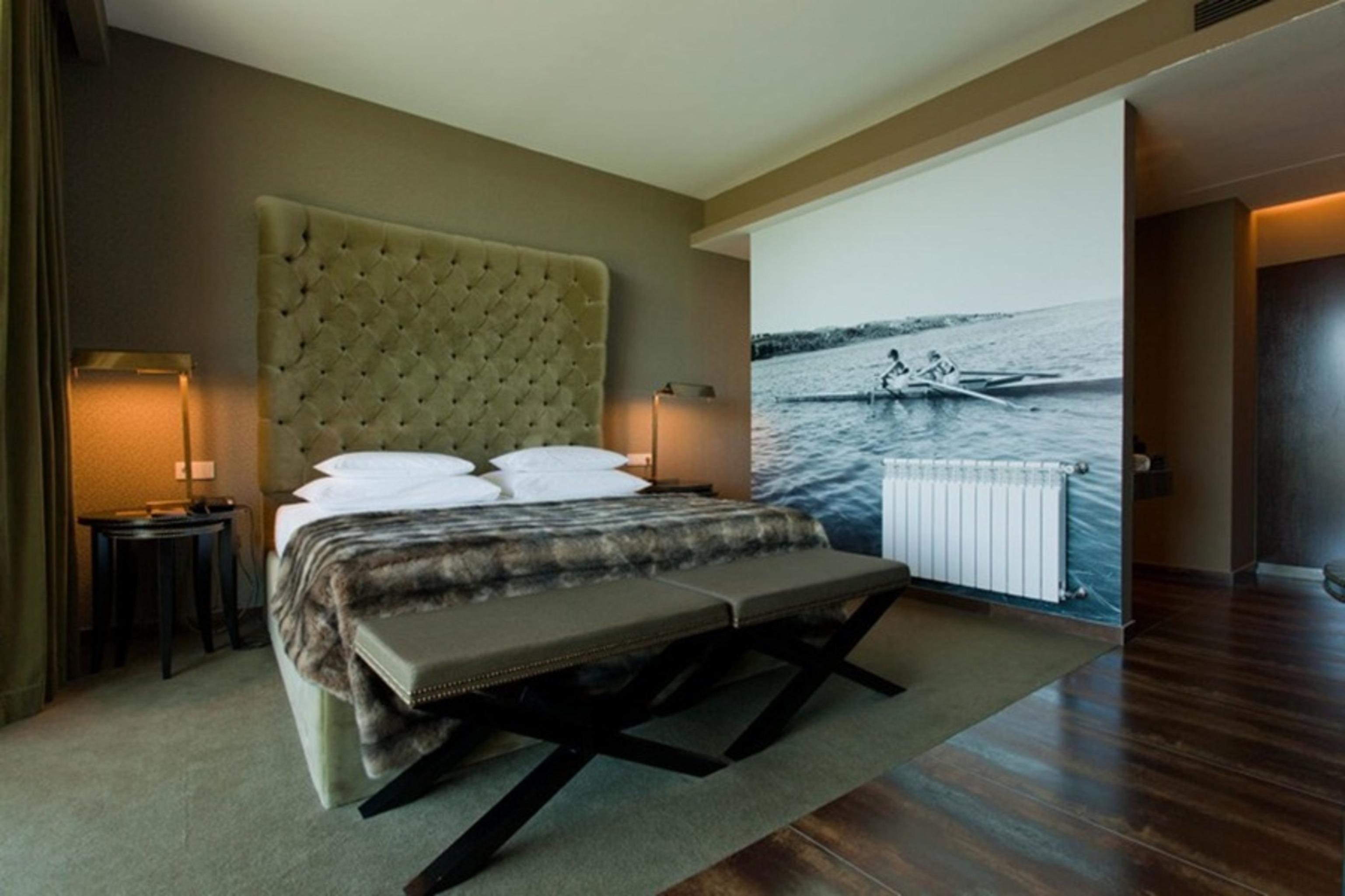 Ap Lago Montargil - Conference & Spa エクステリア 写真 The photo shows a modern hotel room featuring a large bed with a tufted headboard and plush bedding. The color palette is neutral, with shades of green and gray. On one side of the room, there are bedside tables with lamps. A comfortable bench sits a