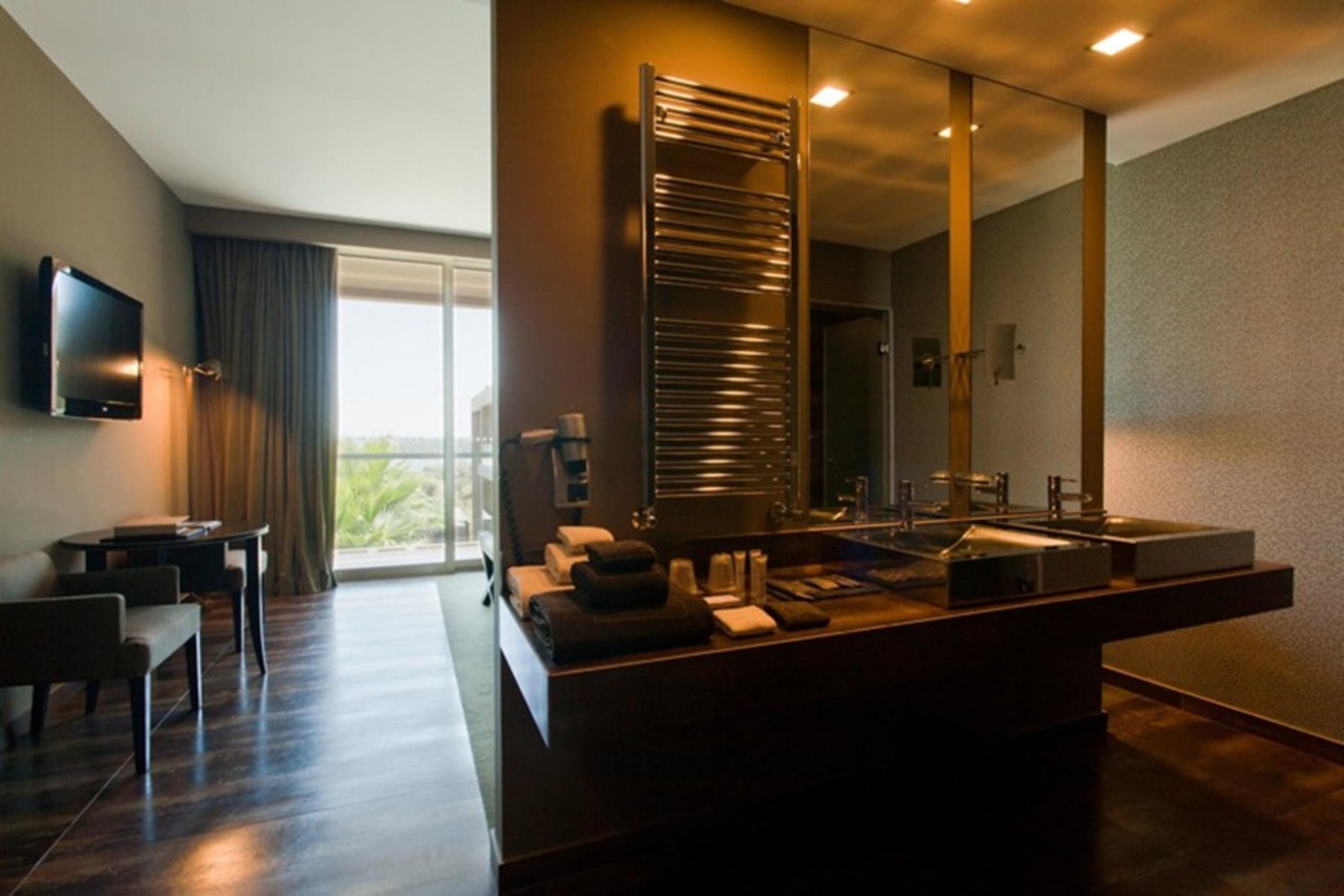 Ap Lago Montargil - Conference & Spa エクステリア 写真 The photo displays a modern hotel room with a contemporary design. The room features a large window, allowing natural light to enter and offering a view outside. On one side, there is a sitting area with a small table and chairs. The other side showc
