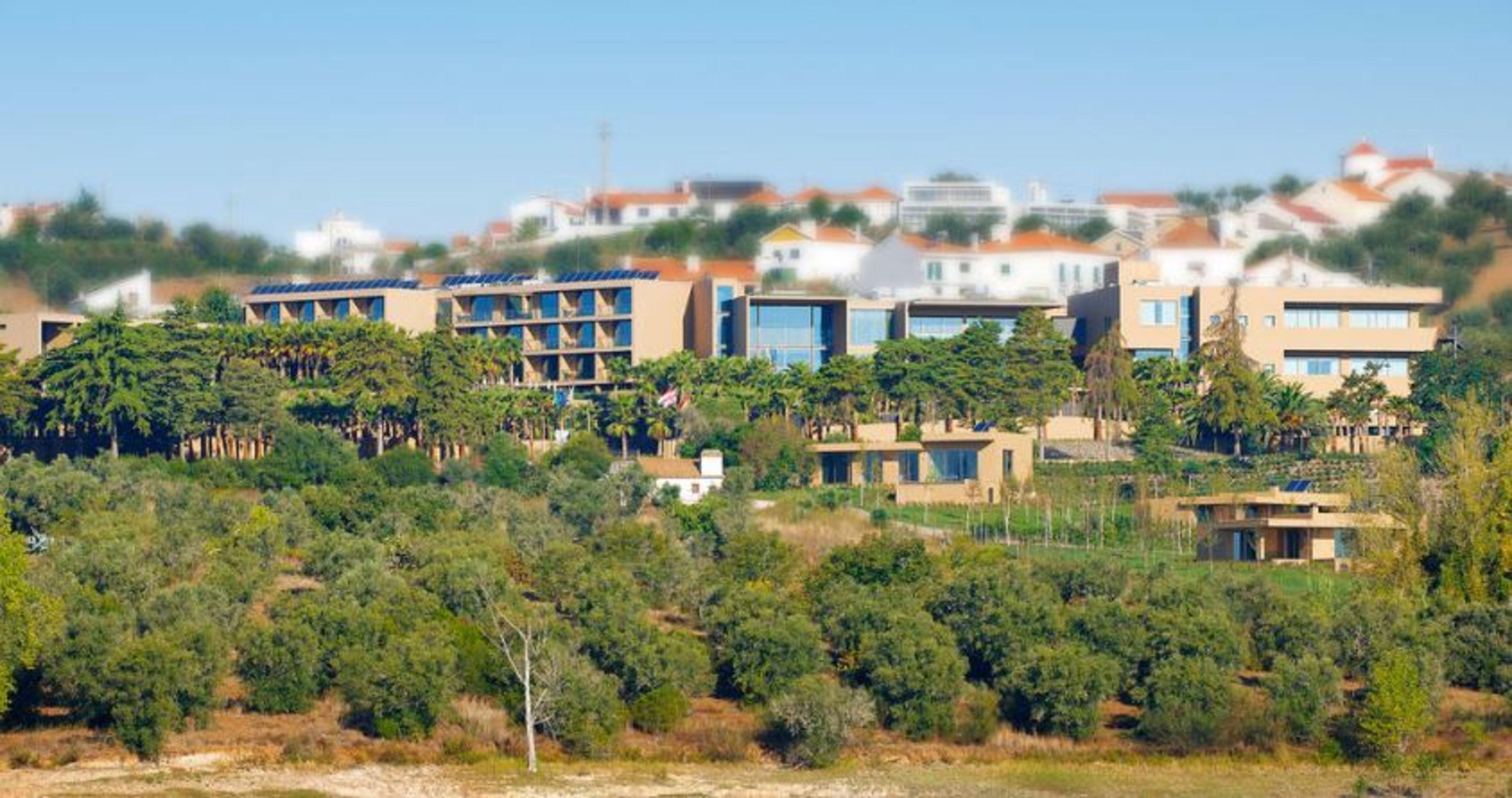 Ap Lago Montargil - Conference & Spa エクステリア 写真 The photo shows a hillside view of a modern resort or hotel complex surrounded by greenery. The buildings are designed with a blend of contemporary architecture and natural elements, featuring wooden accents, large windows, and terraces. In the backg
