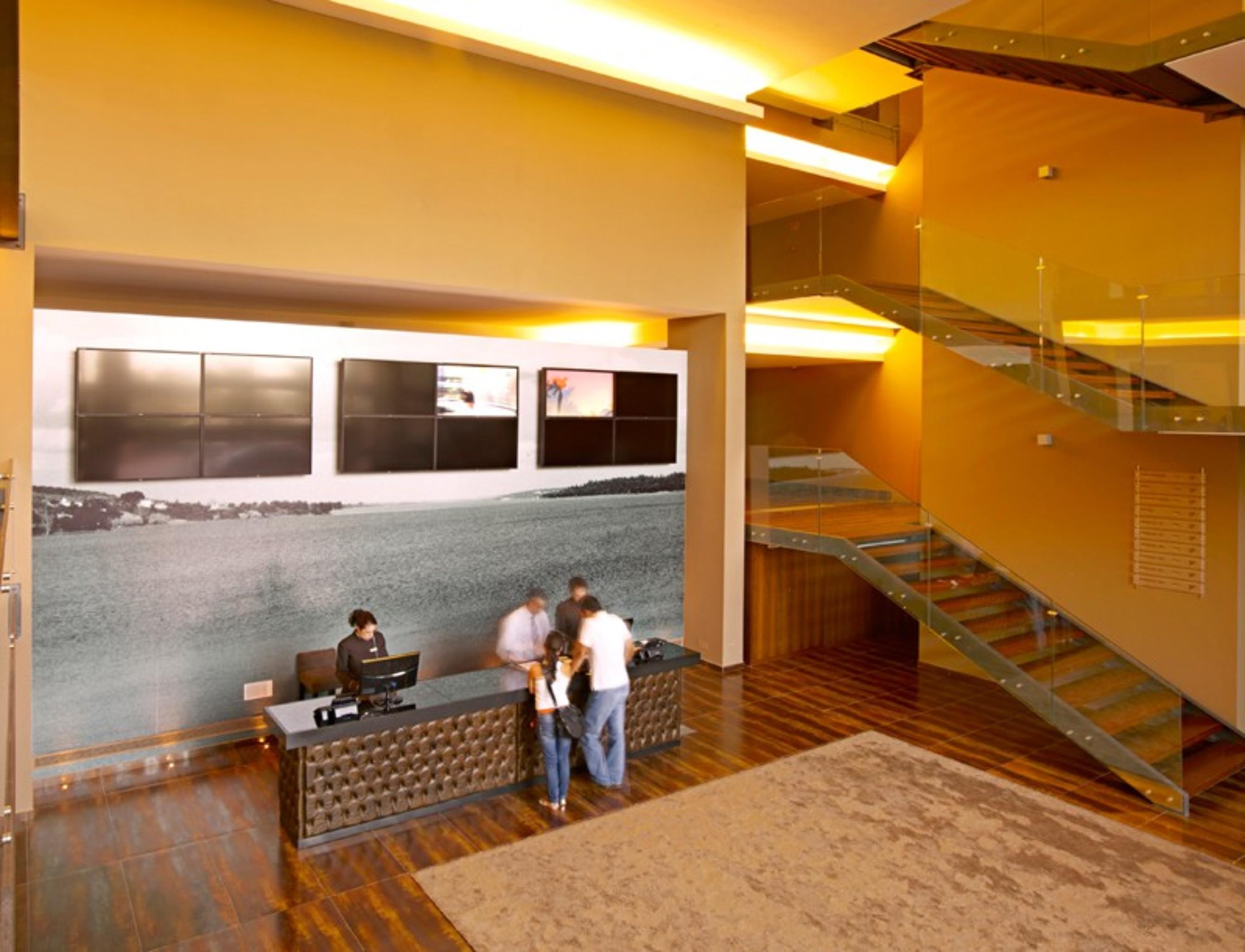 Ap Lago Montargil - Conference & Spa エクステリア 写真 The photo depicts a modern lobby area with a reception desk. The design features a combination of warm colors and wood flooring. In the background, there is a large wall-mounted screen or display, showcasing several monitors. The wall behind the desk