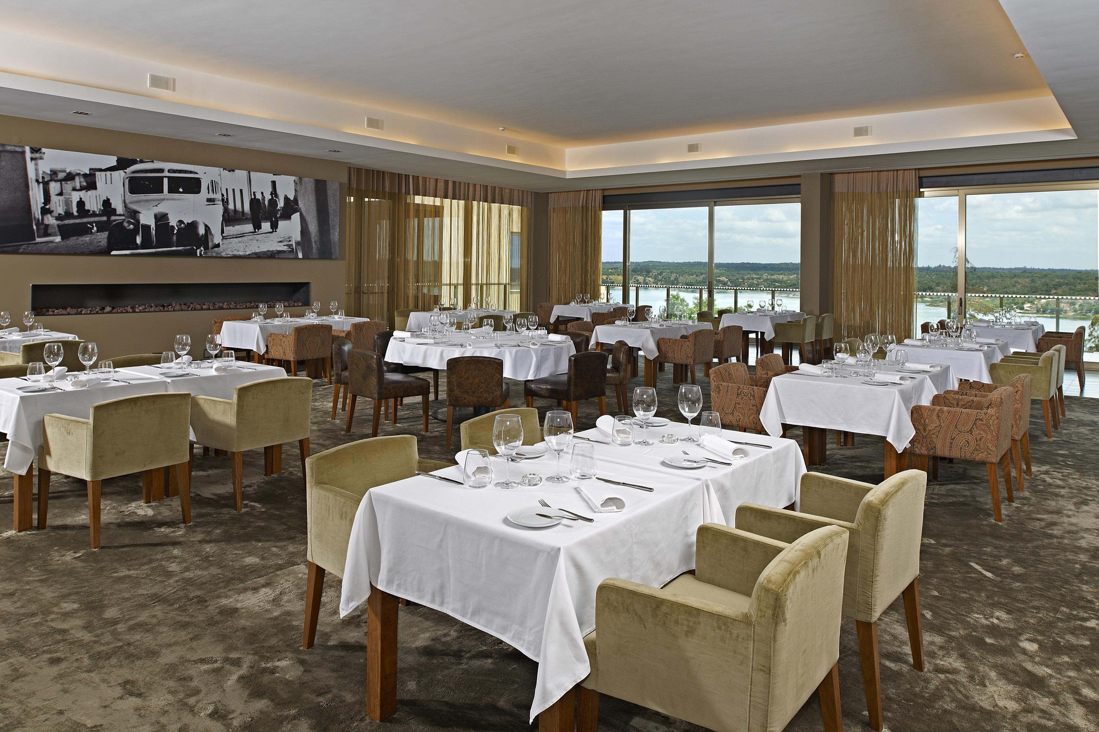 Ap Lago Montargil - Conference & Spa エクステリア 写真 The photo shows an elegant restaurant interior featuring neatly arranged tables with white tablecloths. Each table is set with plates, cutlery, and glasses. The seating includes a mix of upholstered chairs in different colors—some light and others da