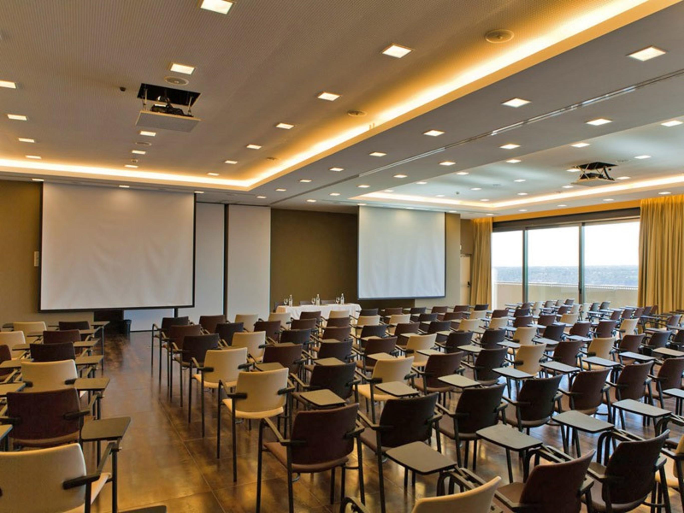 Ap Lago Montargil - Conference & Spa エクステリア 写真 The photo shows a large conference room set up for a presentation or meeting. There are multiple rows of chairs arranged in a semi-theater style, facing two large projection screens. The room has a modern design, with soft lighting and large windows 