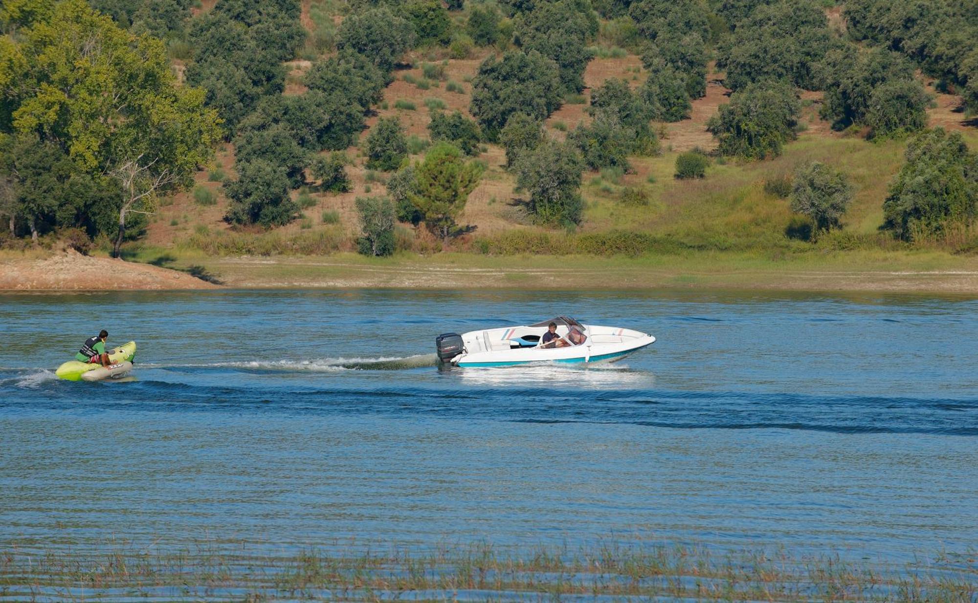Ap Lago Montargil - Conference & Spa エクステリア 写真 The photo shows a scene on a water body, likely a river or lake. In the foreground, a speedboat is moving quickly through the water, leaving a wake behind it. There are two people visible in the boat. In the background, there is a hilly area covered 