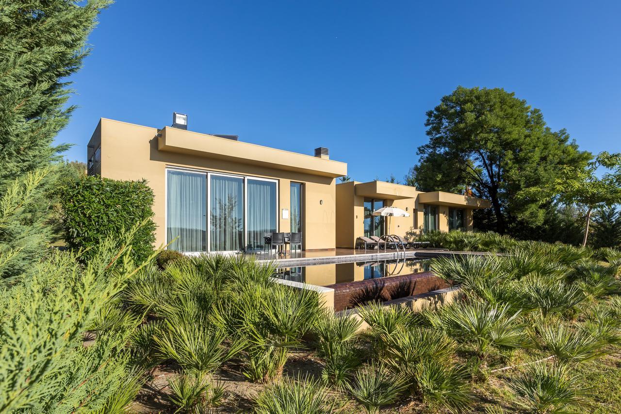 Ap Lago Montargil - Conference & Spa エクステリア 写真 The photo shows a modern villa or house set in a natural landscape. The building features a contemporary design with large glass windows and a beige exterior. In front of the house, there is a pool area, and the surrounding landscape includes greener