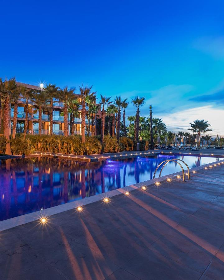 Ap Lago Montargil - Conference & Spa エクステリア 写真 The image shows a serene and inviting outdoor area with a large swimming pool that features a beautiful blue hue, likely illuminated by lights. Surrounding the pool are well-maintained palm trees and lush greenery, creating a tropical atmosphere. In 